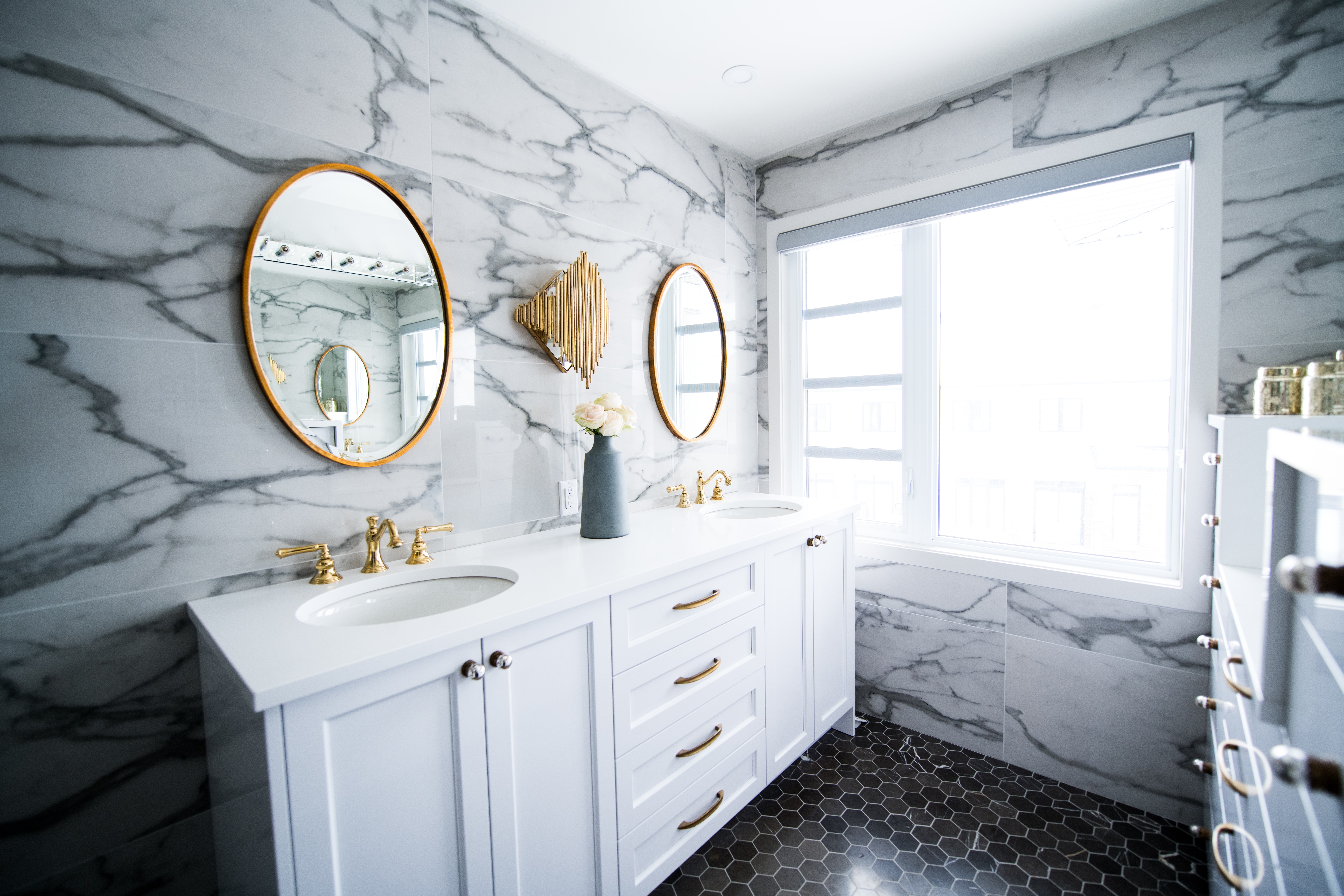 Bright bathroom remodel with white marble, gold accents, two sinks and two mirrors.